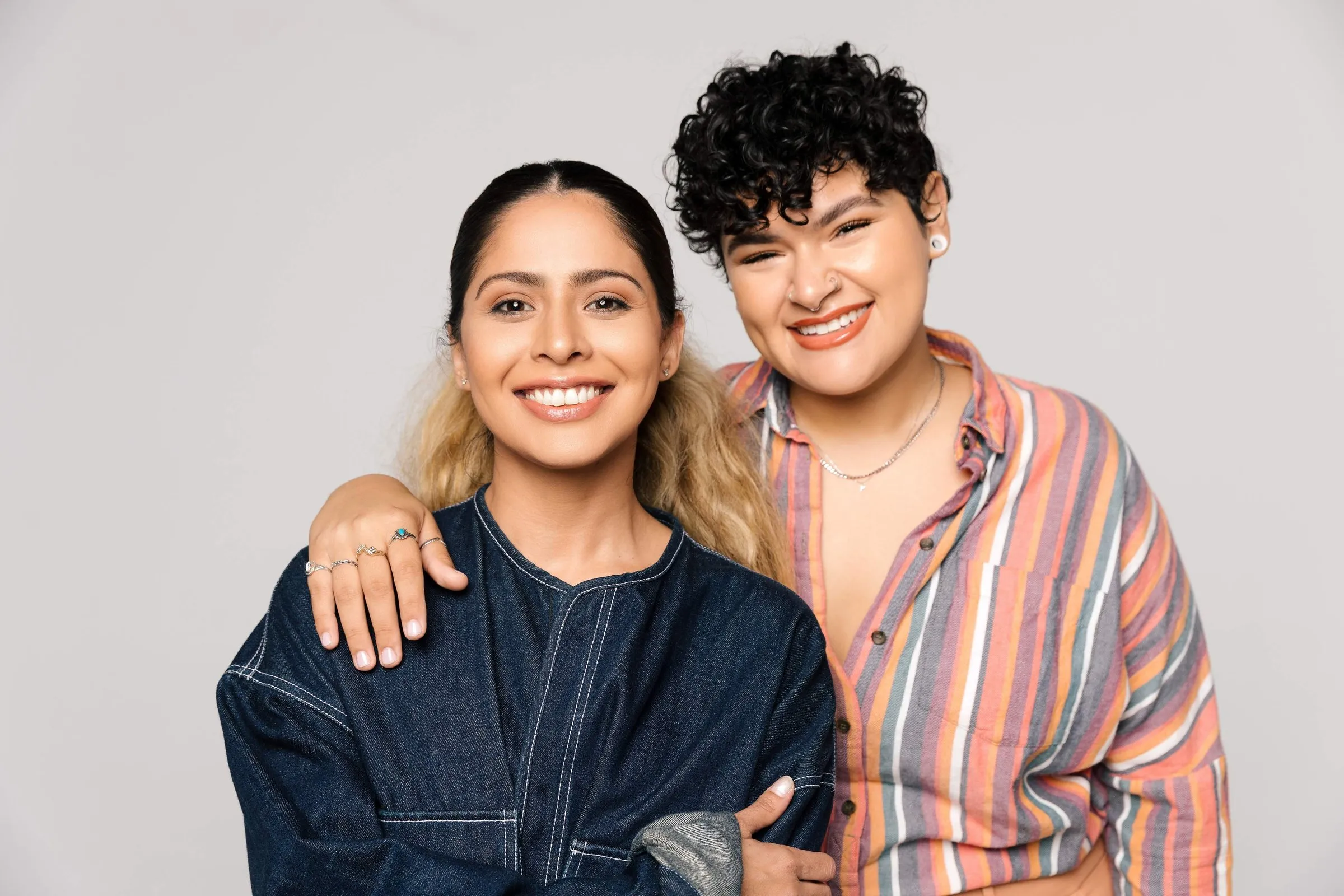 Two smiling young women pose together, one with her arm around the other’s shoulders.
