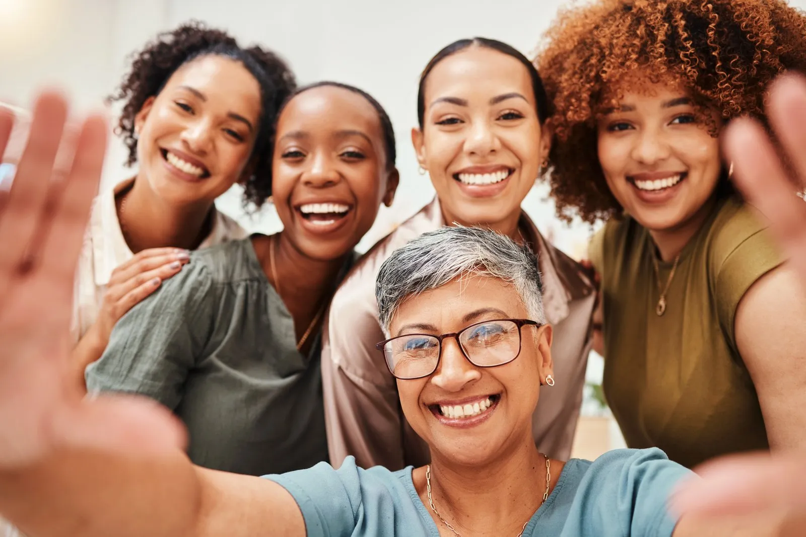 Five smiling women lean in together for a group selfie.