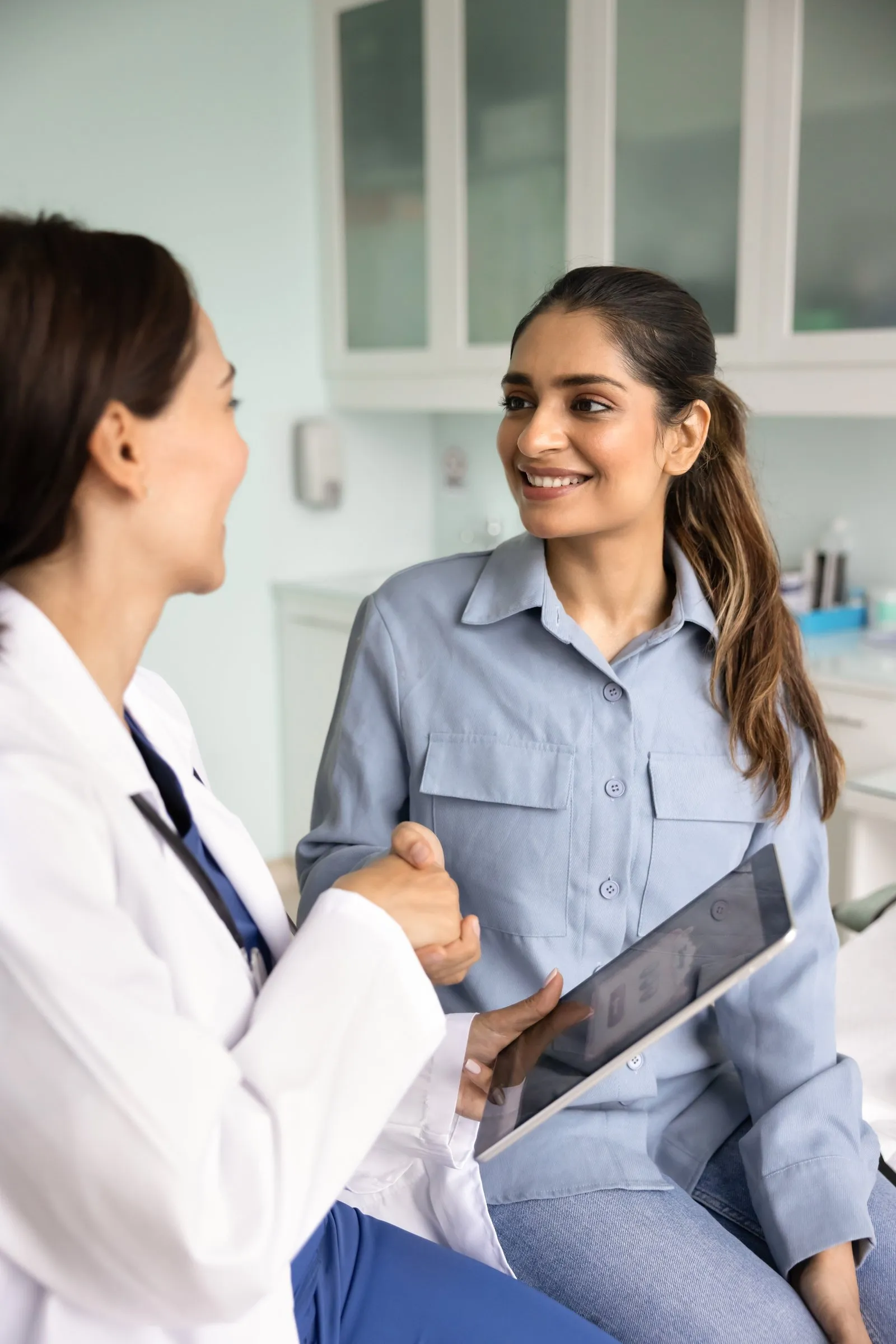 A smiling patient talks with a clinician in a health center exam room.